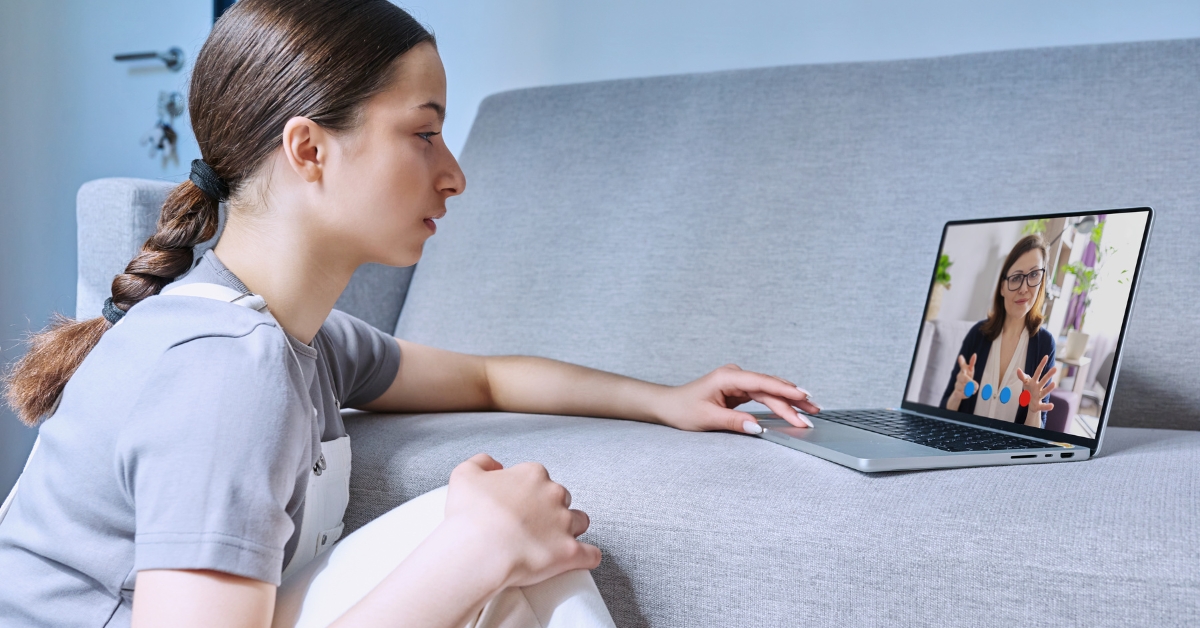 A teen girl having a video call on a laptop, illustrating telehealth for mental health treatment for teens.