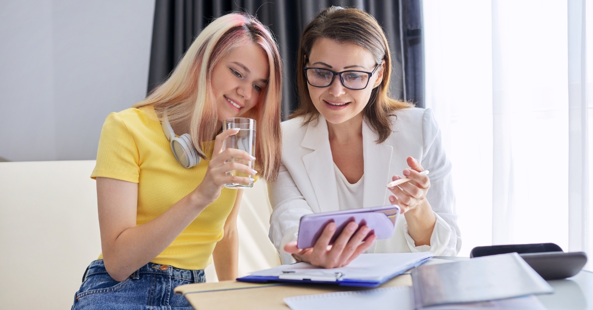 A young woman and her therapist discussing PTSD outpatient treatment while looking at a smartphone, both smiling.