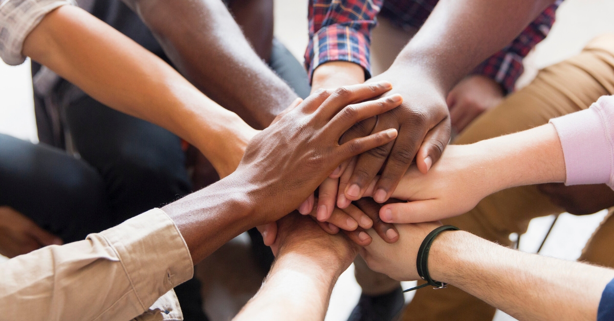 A diverse group of hands stacked together, symbolizing unity and support in group therapy for youth.