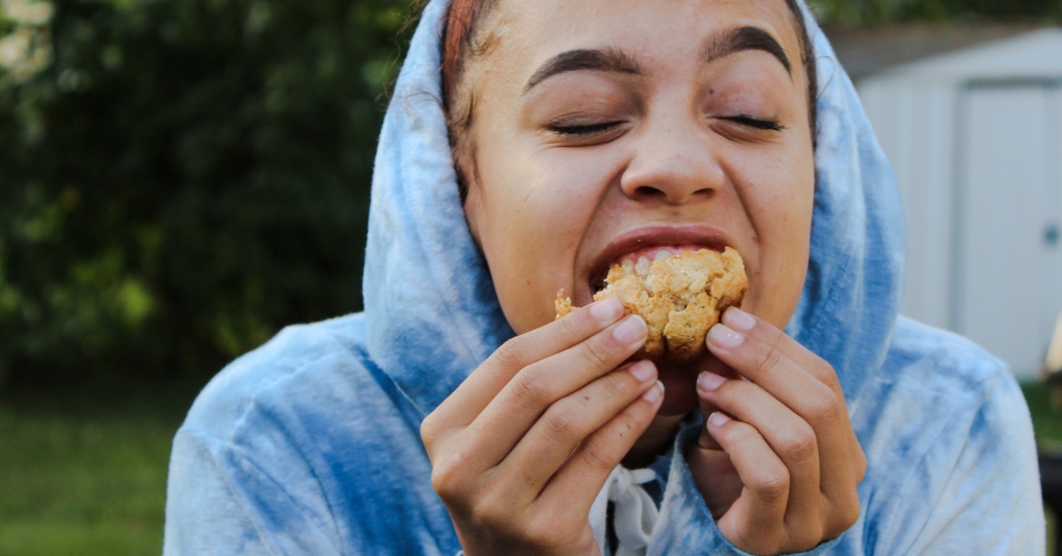 A person in a hoodie eating a cookie with a scrunched face, illustrating Food Aversion on Nutrition and Health.