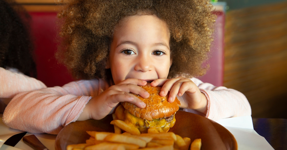 A child with curly hair eats a burger and fries, illustrating ARFID in children.