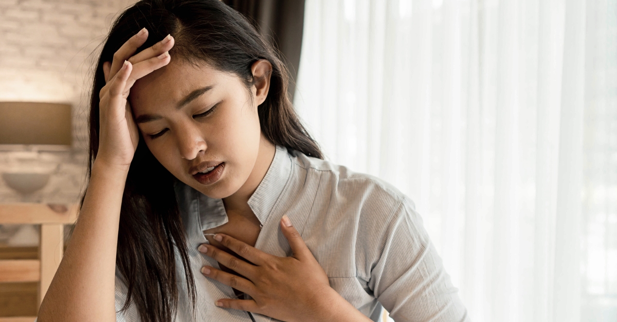 Woman holding her chest and head, appearing distressed, illustrating shortness of breath symptoms.