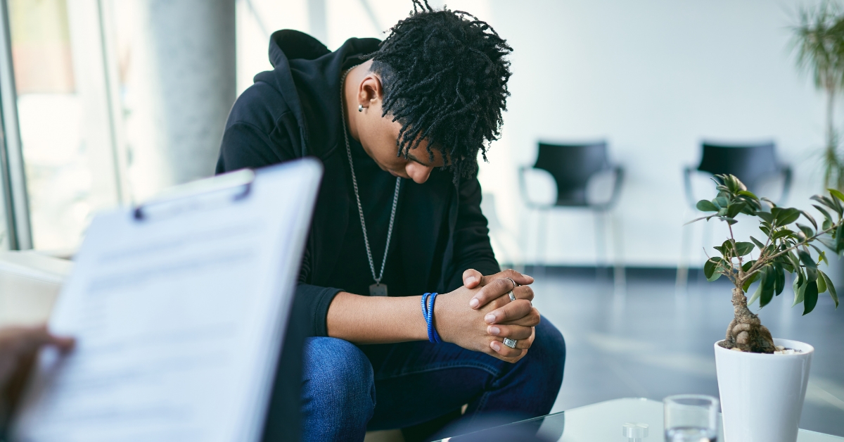 A teen sitting with head bowed in a counseling session, illustrating the benefits of teen outpatient mental health.