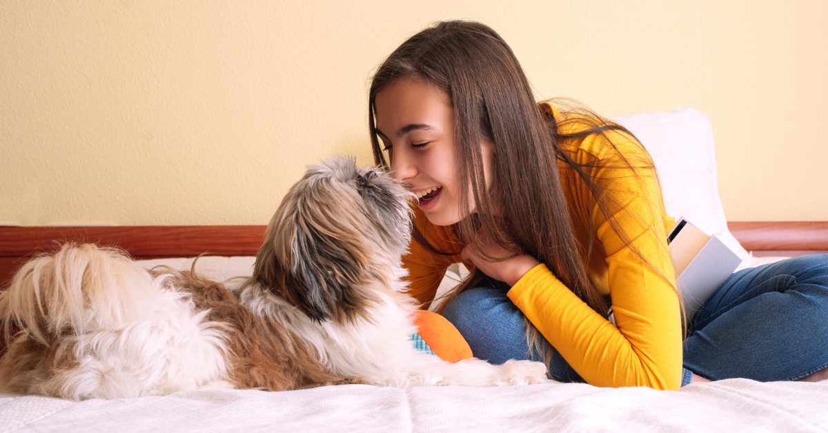 A happy teenage girl on a bed playing with her dog, illustrating the benefits of getting an emotional support animal.