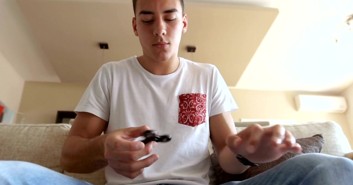 Teenager sitting on a couch, intently spinning a fidget spinner, illustrating the connection between fidgeting and anxiety in adolescents.