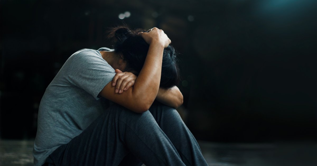 Person sitting with head down and arms crossed, depicting the mental health effects of long-term anxiety.