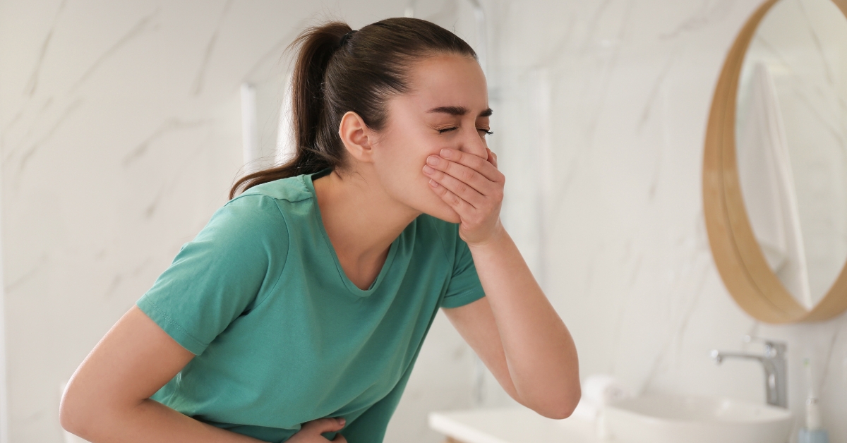 Woman covering her mouth and holding her stomach, clearly experiencing nausea in a bathroom setting.