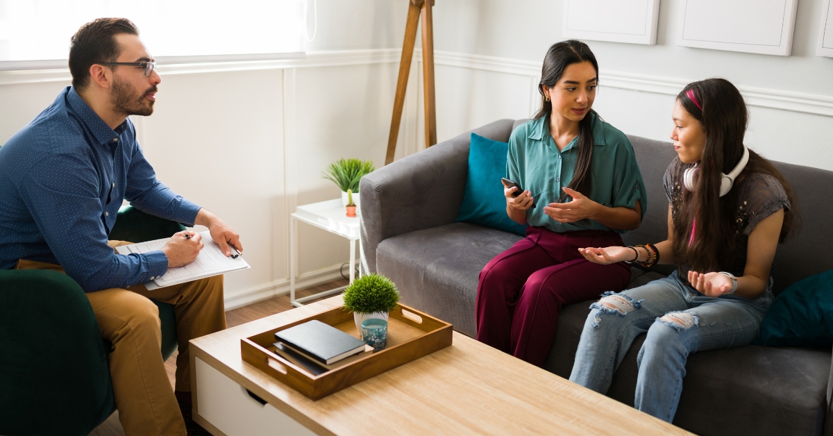 A family therapy session addressing behavioral issues in teens, with a therapist observing the conversation.