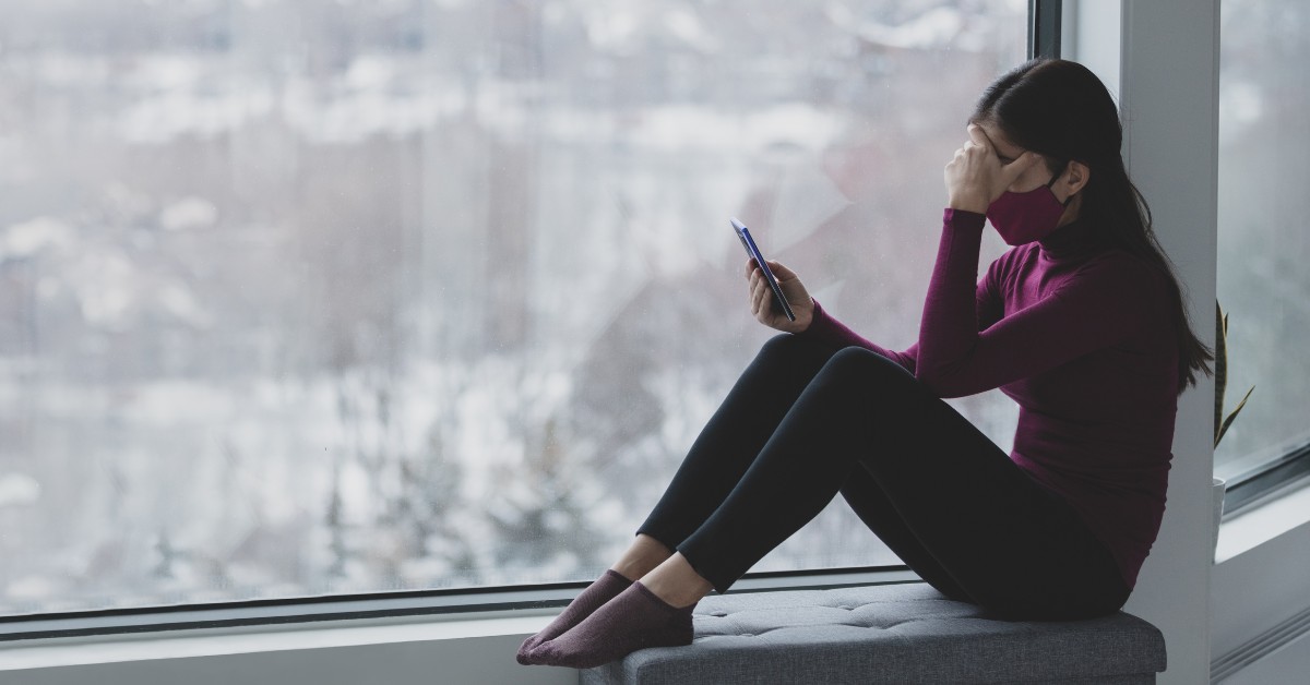 Woman sitting by a window with her face in hand, representing Social Anxiety Disorder: Beyond Shyness.