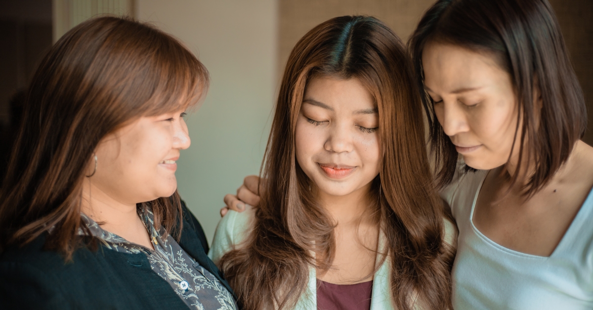 Three women standing close together, offering comfort and illustrating a family supporting mental healing.