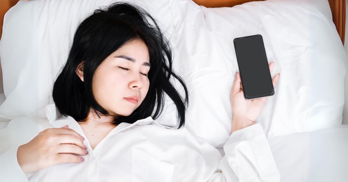 Young woman sleeping peacefully with a phone in hand, emphasizing healthy sleep habits for better mental health.