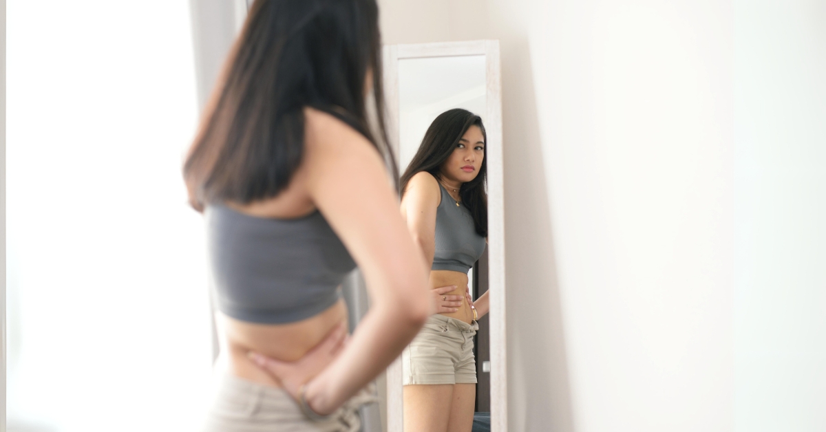 Teenage girl critically examining her body in a mirror, highlighting the impact of social media on body image.