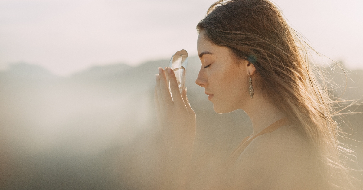 Young woman holding a crystal close to her face in a serene setting, symbolizing trauma-informed youth services.