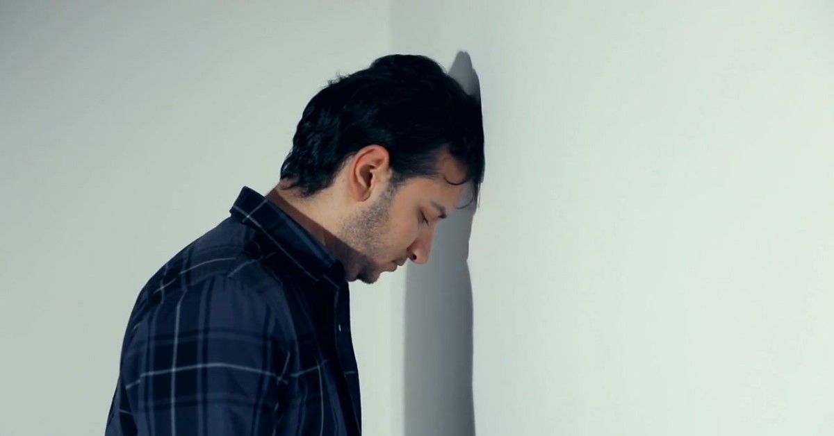 Man with his head against a wall, depicting social life challenges for those with depression.