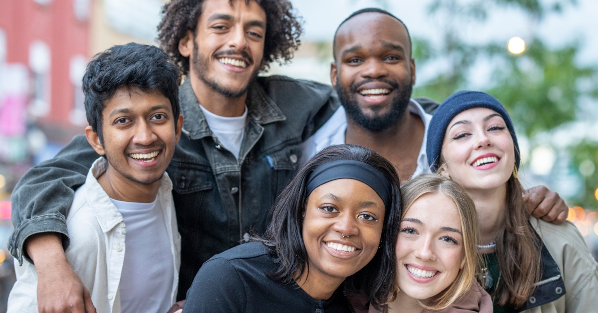 A group of diverse, smiling teens embracing each other outdoors, symbolizing youth services supporting teen mental health.