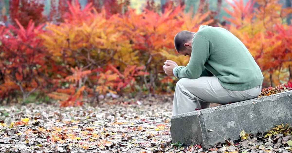 Man sitting outdoors with head down, illustrating environmental factors contributing to anxiety.