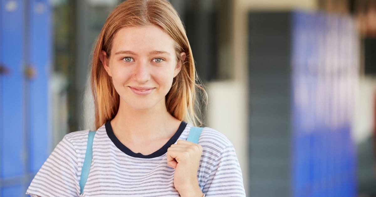 Teenage girl smiling slightly while holding a backpack strap, subtly depicting anxiety in teenage girls.