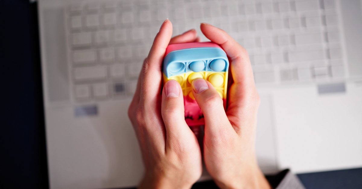 Hands holding a colorful stress toy near a laptop, highlighting technology in anxiety treatment: apps and tools.