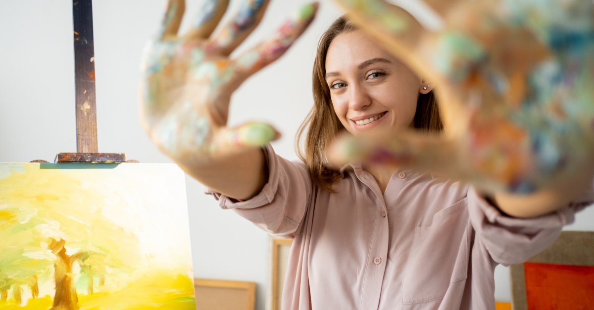 A smiling woman shows her paint-covered hands, illustrating art therapy techniques for anxiety management.