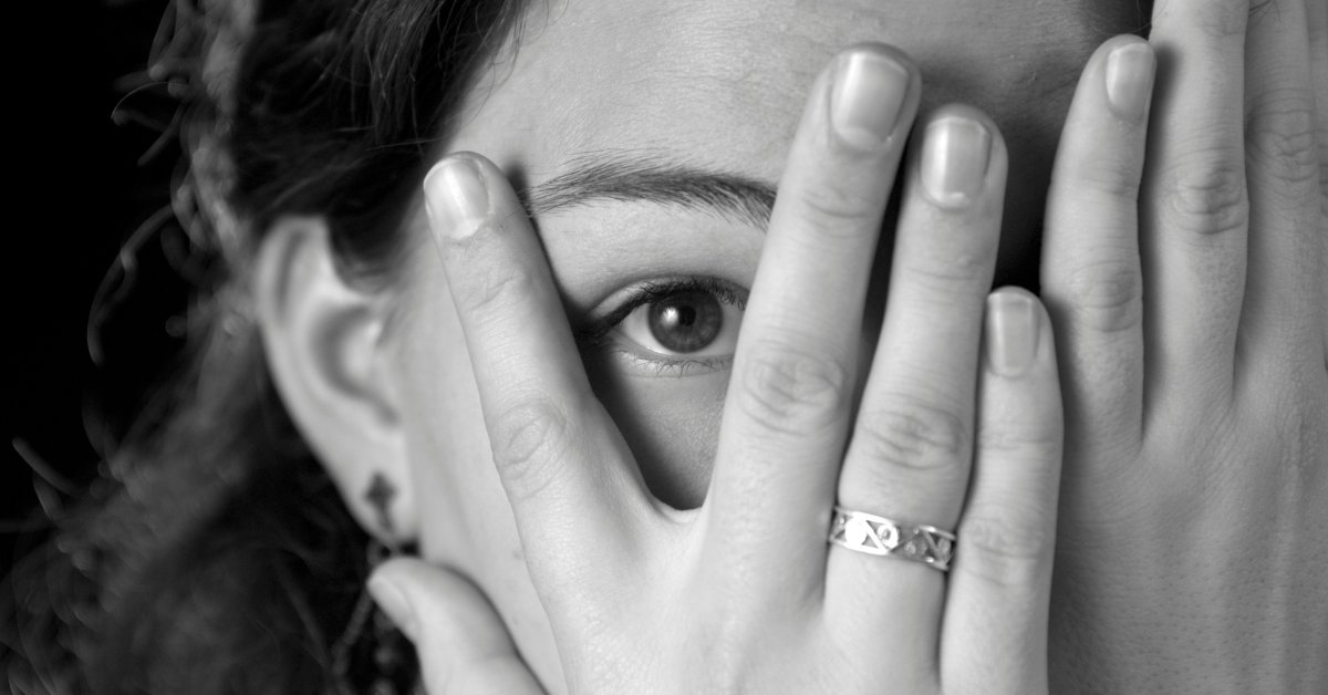 A woman peeking through her hands, symbolizing Exposure Therapy: Facing Fears in Anxiety Treatment.